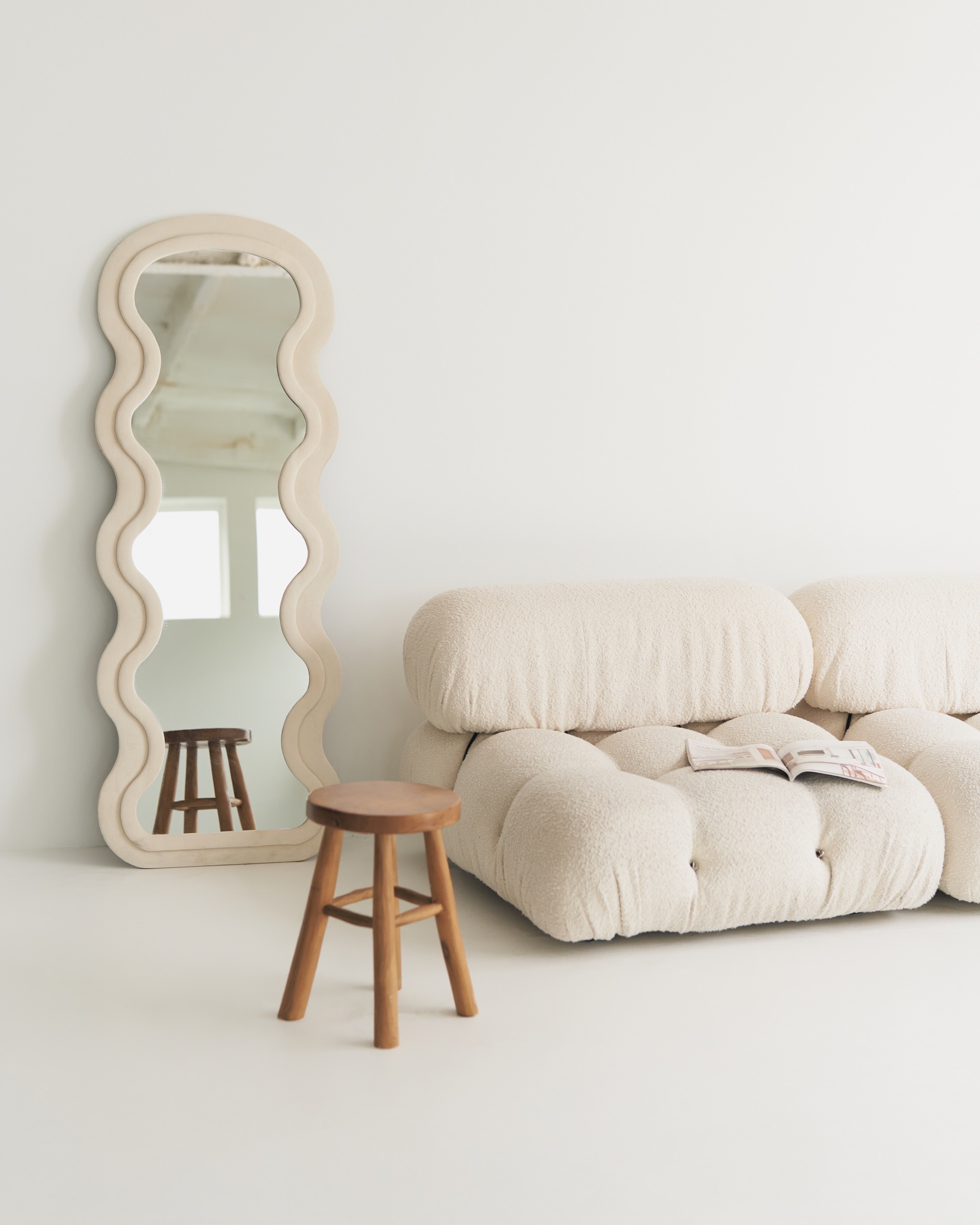 Cream sofa beside a sculptural mirror and wooden stool